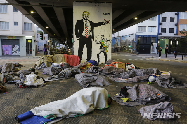 【상파울루( 브라질) = AP/뉴시스】 브라질 상파울루시내의 한 고가도로 아래에서 올 해 7월 자이르 보우소나루 대통령을 트럼프 미 대통령의 꼭둑각시로 묘사한 풍자 벽화아래에서 잠자는 노숙자들.   