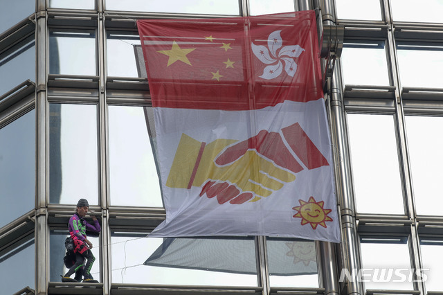【홍콩=AP/뉴시스】프랑스 암벽 및 도심 등반가 알랭 로베르가 16일(현지시간) 홍콩 청쿵 센터 건물에 올라 중국 국기와 홍콩기 그리고 그 아래 중국과 홍콩이 서로 악수하는 그림이 그려진 깃발을 달고 있다.로베르는 "홍콩에 속히 평화와 합의가 이뤄지길 바라는 마음"으로 건물에 올랐다고 밝혔다. 2019.08.16.