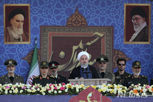 로하니 이란 대통령이 22일 1980년의 이란-이라크 전 개시 39주년 기념 군사퍼레이드에서 연설하고 있다. 1979년 이슬람종교혁명 지도자 아야톨라 호메이니와 현 최고지도자 하메네이 사진이 나란히 걸려있다.  AP 
