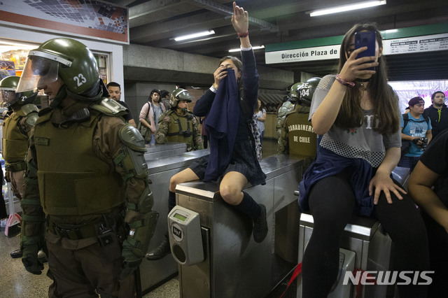 【산티아고=AP/뉴시스】18일(현지시간) 칠레 산티아고의 한 지하철역에서 학생들이 회전식 개찰구를 막고 지하철과 버스 요금 인상에 항의하는 시위를 벌이는 중에 칠레 경찰이 주변에서 대응하고 있다. 2019.10.19.