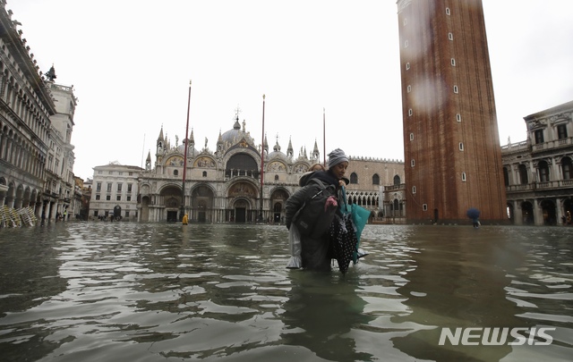 【베네치아=AP/뉴시스】이탈리아 베네치아에서 12일(현지시간) 53년래 최악의 홍수가 발생해 산마르코 광장이 바닷물에 잠겨 있는 가운데 한 여성이 아이를 업고 물을 헤치며 걷고 있다. 2019.11.13