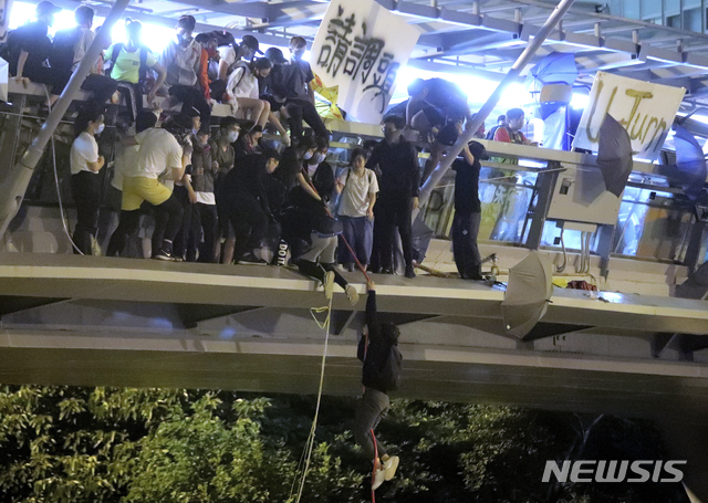 [홍콩=AP/뉴시스]경찰에 포위된 홍콩이공대 안에 갇혀 있는 시위대 일부가 18일 교내를 가로지르는 보행자 전용 고가도로 위에서 밧줄을 이용해 고가 밑 고속도로로 탈출을 시도하고 있다. 수십명의 시위대가 밑에서 오토바이를 타고 기다리던 자원봉사자들이 이들을 태워 도주, 탈출에 성공했다. 2019.11.19