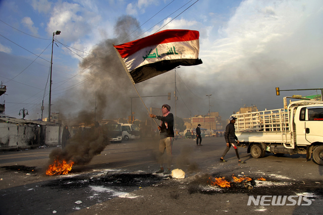 [바그다드=AP/뉴시스]8일(현지시간)  이라크 수도 바그다드의 타흐리르 광장에서 이란의 미군 기지 미사일 공격에 항의하는 시위가 열려 한 남성이 불 타는 도로에서 이라크 국기를 흔들고 있다. 이란은 이날 새벽 솔레이마니 사령관을 사살한 미국의 공습에 대한 보복으로 이라크 내 두 곳의 미군 기지에 미사일 공격을 감행했다. 2020.01.08.