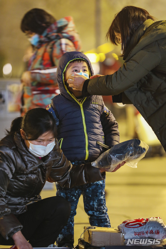 [우한=AP/뉴시스]21일(현지시간) 중국 후베이성 우한의 한커우 기차역에서 한 여성이 어린이의 마스크를 고쳐 씌워주고 있다.2020.01.22.