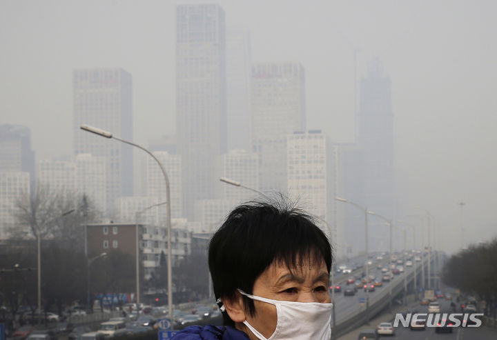 [베이징=AP/뉴시스]사진은 2015년 12월20일 스모그로 뒤덮인 베이징 중심업무지구의 사무실 건물들 속에서 오염 방지용 마스크를 쓴 여성이 육교 위를 걷는 모습. 2023.12.08.