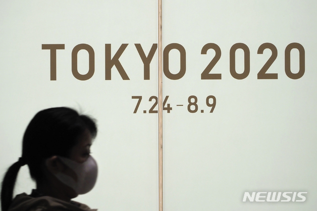 [도쿄=AP/뉴시스]13일(현지시간) 일본 도쿄에서 마스크를 낀 한 여성이 도쿄 2020 올림픽을 홍보하는 화면 앞을 지나고 있다. 2020.03.14.
