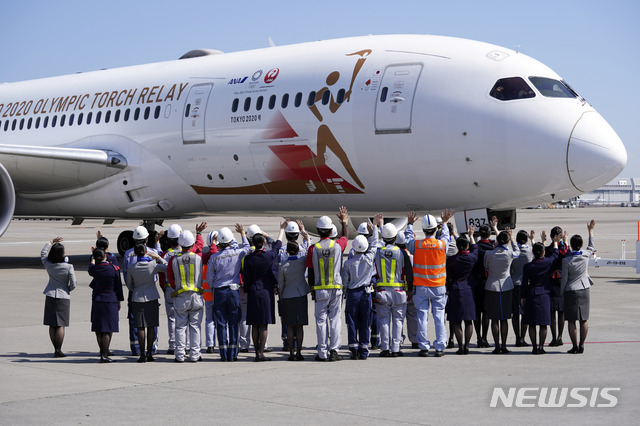 [도쿄=AP/뉴시스]18일 일본 도쿄 하네다 국제공항 활주로에서 지상 근무자들이 2020 도쿄 올림픽 성화 운반차 그리스로 떠나는 일본 항공 소속 특별기를 향해 손을 흔들며 환송하고 있다. 2020.03.18.  