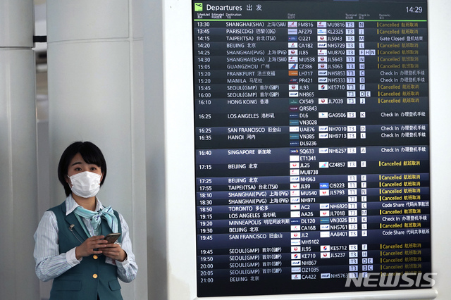 [도쿄=AP/뉴시스]지난 2020년 2월18일 일본 도쿄 하네다 공항에 마스크를 쓴 직원이 신종 코로나바이러스 감염증(코로나19)로 취소된 항공 스케줄을 표시한 전광판 옆에 서 있다. 2020.03.19.