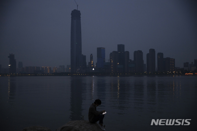 [우한=AP/뉴시스]4월5일(현지시간)  신종 코로나바이러스 감염증(코로나19)이 처음으로 발생했던 중국 후베이성 우한시의 강가에서 한 남성이 휴대전화를 보고 있다. 2020.05.05.
