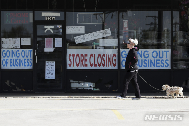 A woman takes walk with a dog in front of the closing signs displayed in a store&#039;s window front in Niles, Ill., Wednesday, May 13, 2020. (AP Photo/Nam Y. Huh)