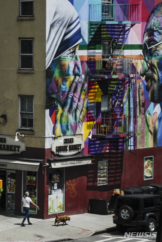 [뉴욕=AP/뉴시스]16일(현지시간) 테레사 수녀와 마하트마 간디 벽화가 그려진 미국 뉴욕의 10번가에서 한 여성이 반려견과 함께 산책하고 있다. 2020.07.17.