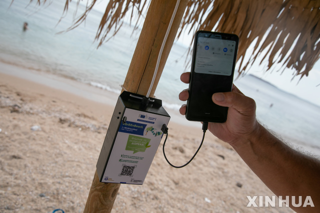 [아테네=신화/뉴시스]21일(현지시간) 그리스 아테네 남부의 바리불라불리아그메니 시청 근처 해변의 그늘막에 설치된 태양광 충전기에서 한 남성이 휴대폰을 충전하고 있다. 2020.07.22