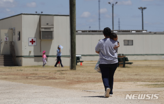 [딜리( 미 텍사스주)= AP/뉴시스]미 텍사스주 딜리에 있는 이민가족 수용소 안에서 아이를 안은 엄마가 걸어가고 있다. 미 이민국은 지난 6월 지역 법원이 코로나19의 위험을 지적하며 아이들의 석방을 명령했지만 이에 따르겠다면서도 100여명의 어린이들을 계속 수용하고 있다.   