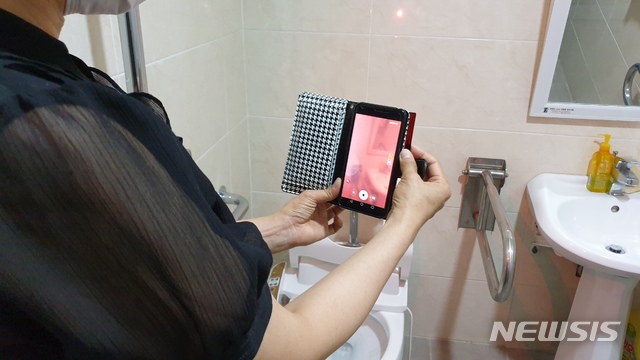 [창원=뉴시스] 한 여성이 화장실에서 휴대폰에 '불법카메라 간이 탐지카드'를 덧대 불법카메라 설치 여부를 점검하고 있다. (사진=경남도 제공) 2020.08.12. photo@newsis.com 