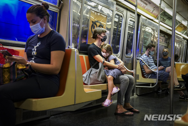 [뉴욕=AP/뉴시스]뉴욕의 지하철 안에서 마스크를 쓴 한 여자아이가 엄마의 무릎에 앉아 쉬고 있다. 띄엄띄엄 앉은 승객들 모두 마스크를 착용하고 있다. 2020.8.18