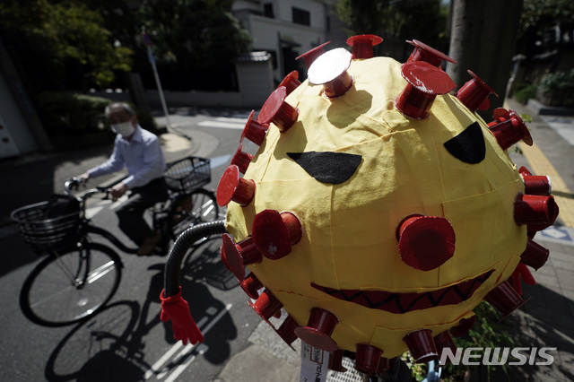[도쿄=AP/뉴시스]지난 28일 일본 도쿄의 한 거리에서 코로나19 확산 예방을 위해 마스크를 쓴 한 남성이 코로나바이러스를 형상화한 허수아비 옆을 자전거로 지나고 있다. 2020.09.28.