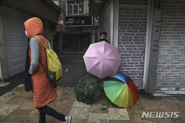 [AP/뉴시스] 11월22일 이란 수도 테헤란에서 문닫힌 가게 앞에 한 우산 행상이 서 있다. 이란은 다시 상점 폐쇄와 대도시 간 이동 금지령을 내렸다.   