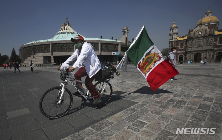 [멕시코시티=AP/뉴시스]2020년 11월 24일 멕시코시티 과달루페 대성당 앞 광장에서 한 순례자가 멕시코 국기를 휘날리며 자전거를 타고 있다. 2022.06.22