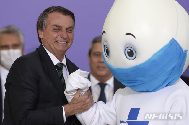 [브라질리아=AP/뉴시스]자이르 보우소나루 브라질 대통령이 브라질리아 플라날투 대통령궁에서 코로나19 백신 접종 계획을 발표하면서 백신 접종 캠페인 마스코트와 사진을 찍고 있다.2020.12.17.