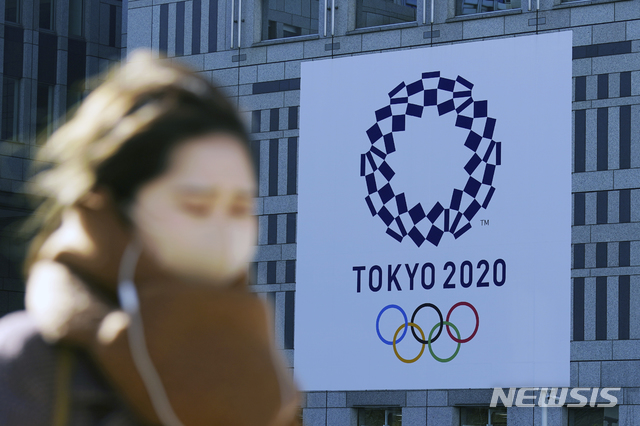 [도쿄=AP/뉴시스]19일 코로나19 예방을 위해 마스크를 쓴 한 여성이 일본 도쿄에서 2020 도쿄 올림픽 현수막 근처를 걷고 있다. 도쿄에서는 이날 1240명의 코로나19 신규 확진자가 보고됐다. 2021.01.19. 