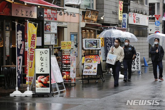 [도쿄=AP/뉴시스]8일 일본 도쿄에서 코로나19 확산 방지를 위해 마스크를 쓴 시민들이 술집과 식당이 즐비한, 거의 텅 빈 거리를 걷고 있다. 일본 수도권은 이날부터 21일까지 코로나19 확산 억제를 위한 긴급사태 연장에 들어간다. 2021.03.08.