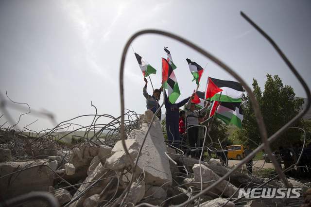 [서안지구=AP/뉴시스]10일(현지시간) 팔레스타인 서안 지구의 한 마을에서 젊은이들이 이스라엘군이 무허가라며 철거한 주택 잔해 주변에 모여 국기를 흔들고 있다. 2021.03.11. 