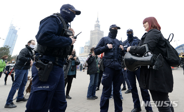 {AP/뉴시스] 3월26일 폴란드 수도 바르샤바에서 경찰들이 마스크를 안 쓴 여성을 제지하고 벌금부과를 위해 이름과 주소를 묻고 있다