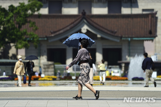 [도쿄=AP/뉴시스]21일 일본 도쿄에서 코로나19의 확산을 막기 위해 마스크를 쓴 한 시민이 양산을 쓰고 거리를 걷고 있다. 2021.04.21.