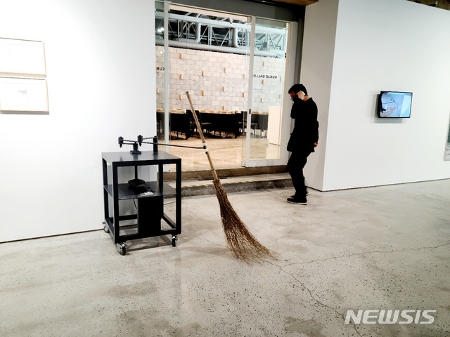[서울=뉴시스] 국제갤러리 부산점에서 열리는 안규철 개인전 '사물의 뒷모습' 전시 장면. 싸리 빗자루가 기계에 달려 좌우로 움직이며 바닥을 쓴다. 