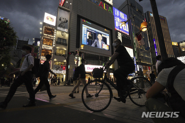 [도쿄=AP/뉴시스]지난 17일 일본 도쿄의 밤 거리를 마스크를 착용한 시민들이 지나가고 있다. 건물의 대형 스크린에는 스가 요시히데 총리의 기자회견이 생중계되고 있다. 2021.06.22. 