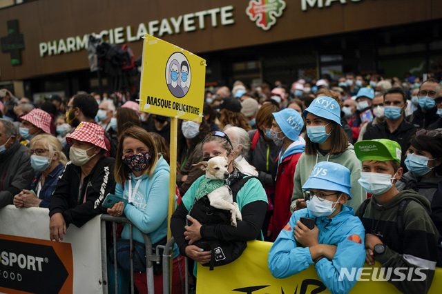 A sign reads &quot;face mask obligatory&quot; as people watch the riders line up for the start of the seventeenth stage of the Tour de France cycling race over 178.4 kilometers (110.9 miles) with start in Muret and finish in Saint-Lary-Soulan Col du Portet, France, Wednesday, July 14, 2021. (AP Photo/Daniel Cole)