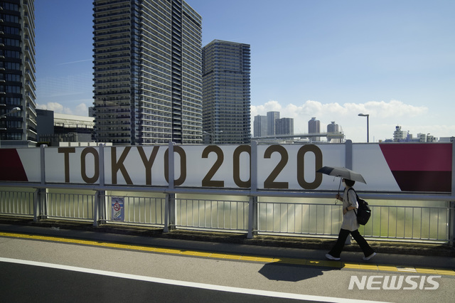 [도쿄=AP/뉴시스]23일 도쿄 올림픽 개막을 6일 앞두고 17일 한 여성이 '도쿄 올림픽 2020'이라는 현수막이 아직도 붙어 있는 도쿄의 한 교량을 지나가고 있다. 도쿄 올림픽 조직위원회는 17일 올림픽촌에 입촌한 사람 가운데 처음으로 코로나19 양성 반응자가 발생했다고 밝혔다. 2021.7.17