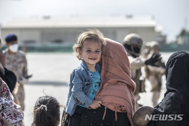 [카불=AP/뉴시스] 21일(현지시간) 아프가니스탄 카불의 하미드 카르자이 국제공항에서 한 아프간 어린이가 엄마 품에 안겨 수송기 탑승을 기다리며 천진난만한 미소를 짓고 있다. 2021.08.23