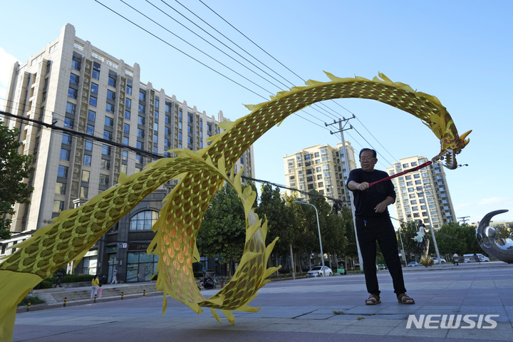 [베이징=AP/뉴시스]한 시민이 지난 9월21일 베이징의 헝다(恒大, 에버그란데) 그룹이 지은 위징베이 아파트 단지 앞에서 천으로 만든 용을 돌리고 있다. 2021.10.15
