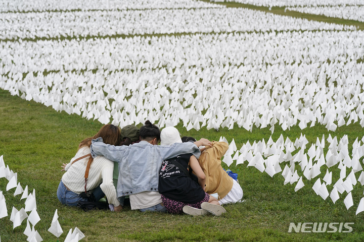 [AP/뉴시스] 21일 미국 워싱턴의 내셔널 몰에 설치된 코로나19 사망자 추모의 흰 깃발 예술품 '아메리카에서' 잔디밭에 방문객들이 서로 어깨를 겯고 앉아있다. 미국에서ㄴ만 67만 명이 사망했다