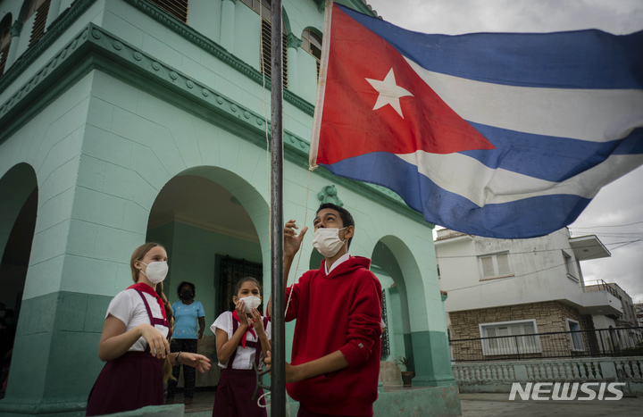 [아바나=AP/뉴시스] 8일(현지시간) 쿠바 아바나에서 학교 재개교 첫날, 한 학교에서 학생들이 국기가 비에 젖지 않게 하기하고 있다. 쿠바 정부가 오는 15일로 예정된 코로나19 봉쇄 완전 해제를 앞두고 아이들을 학교로 다시 돌아가게 하는 것이 우선순위 중 하나라고 밝혔다. 2021.11.09.