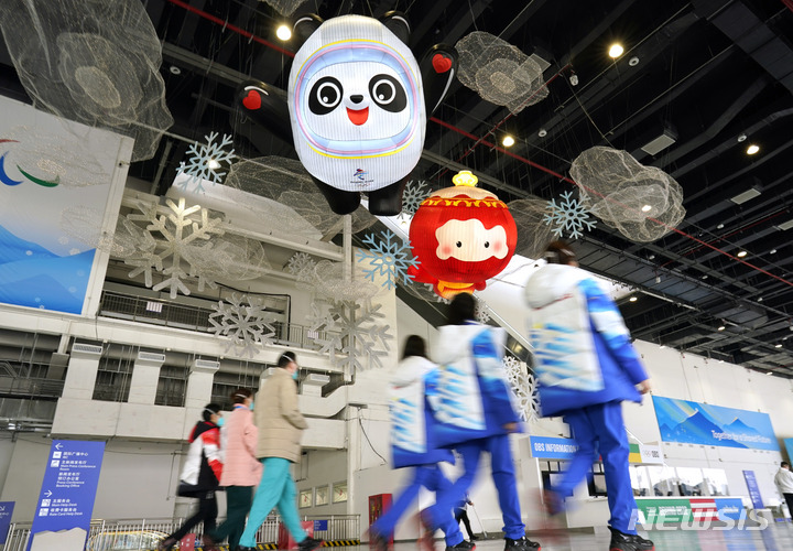 [베이징=AP/뉴시스] 베이징 동계올림픽 자원봉사자들이 지난 18일 중국 베이징 미디어 센터에서 마스코트 앞을 지나가고 있다. 2022.01.20.