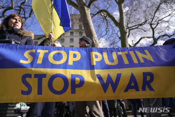 [런던=AP/뉴시스]24일(현지시간) 영국 런던 총리관저 근처에서 우크라이나 지지 시위가 열렸다. 현수막에 블라디미르 푸틴 러시아 대통령과 전쟁을 멈추라는 문구가 적혔다. 2022.2.24.