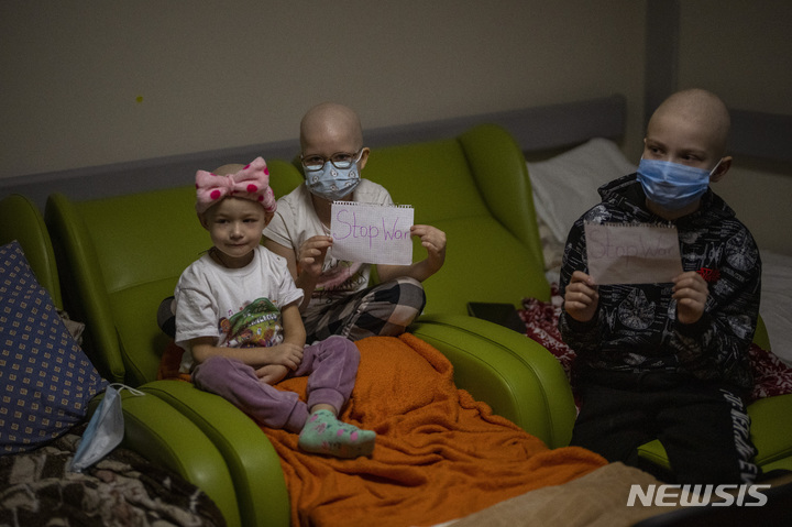 [키예프/AP=뉴시스] 지난 2월28일 우크라이나 키이우 중부에 위치한 오흐마데트 아동병원 지하실에서 소아암 환아들이 '전쟁 중지'라는 문구가 적힌 종이를 들고 있다. 2022.03.01.