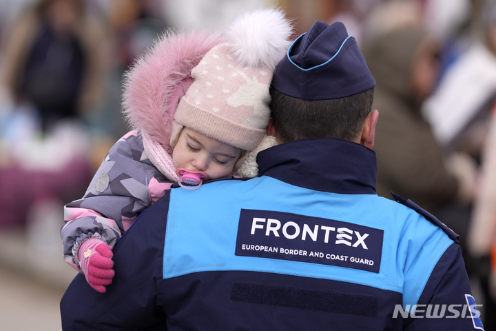 [비스네네메케(슬로바키아)=AP/뉴시스]유럽 국경·해안경비청(FRONTEX·프론텍스) 대원이 지난 3월1일 슬로바키아 비스네 네메케 국경을 넘은 우크라이나 난민이 도착하자 아이를 안고 지나고 있다. 2022.06.14.photo@newsis.com