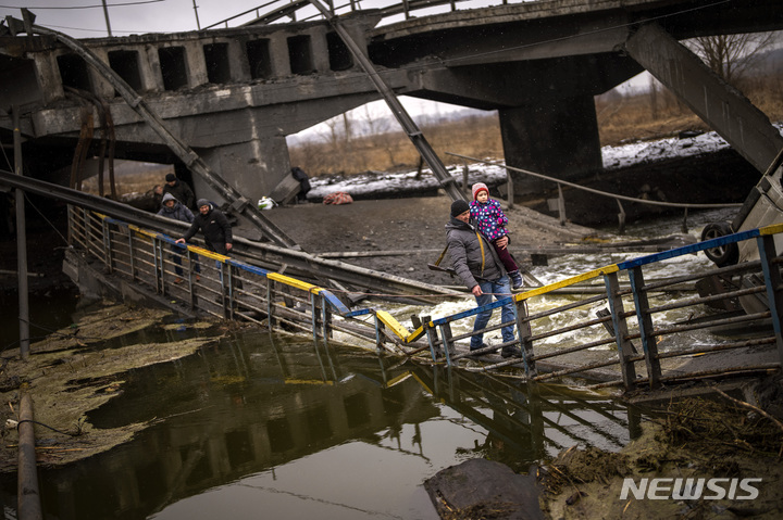 [키이우=AP/뉴시스] 2일(현지시간) 우크라이나 수도 키이우에서 한 지역 민병대원이 대피하는 주민을 도와 어린이를 안고 포격으로 파손된 다리를 건너고 있다. 2022.03.03.