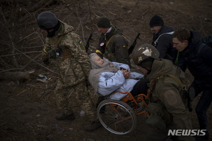 [이르핀=AP/뉴시스] 7일(현지시간) 우크라이나 키이우 외곽의 이르핀에서 우크라이나군 병사들이 러시아군의 포성이 들려오는 속에서 한 노인의 휠체어를 들어 피란을 돕고 있다. 2022.03.08.