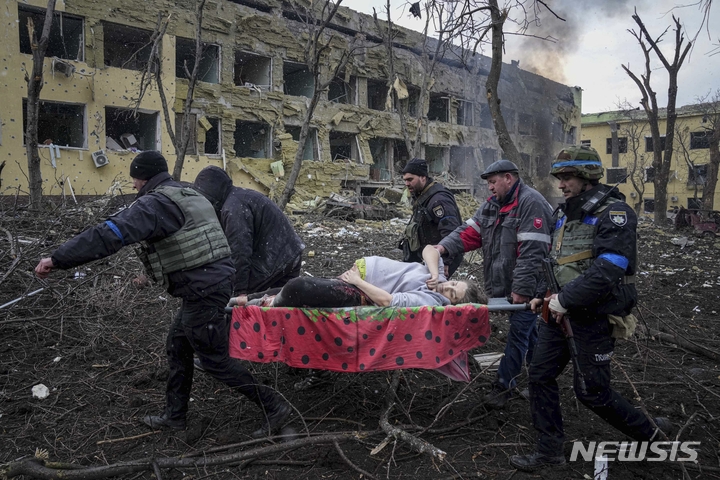 [마리우폴=AP/뉴시스] 9일(현지시간) 우크라이나 마리우폴에서 산부인과 병원이 러시아군의 포격을 받아 응급 구조요원과 자원봉사자들이 부상한 임신부를 옮기고 있다. 볼로디미르 젤렌스키 우크라이나 대통령은 "아이들과 사람들이 병원 잔해에 깔려 있다"라며 이번 공격을 "잔혹 행위"라고 비난했다. 2022.03.10.