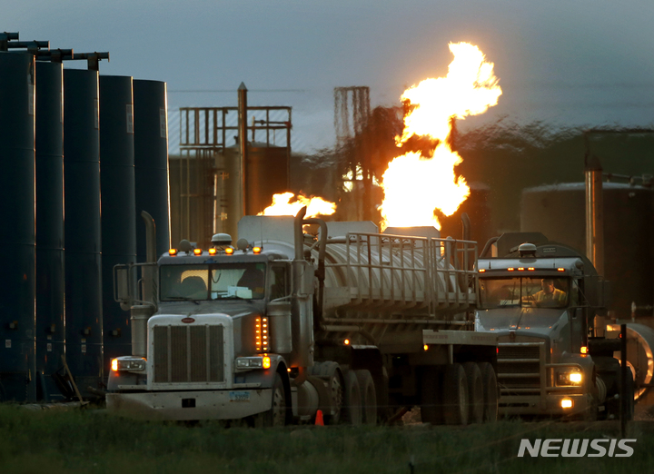 [윌리스턴(미 노스다코다주)=AP/뉴시스]미 노스캐롤라이나주 윌리스턴에서 지난 2014년 6월9일 물과 유압 파쇄 액체를 운반할 대형 트럭들이 천연가스를 태우는 화염을 내뿜는 저장 탱크 앞에 줄지어 서 있다. 미 증권거래위원회(SEC)가 21일(현지시간) 기후 변화에 대처하기 위한 미 정부 노력의 일환으로 기업들에 온실가스 배출량과 기후 위험이 그들의 비즈니스에 미치는 영향을 공개하도록 하는 새로운 규정을 제안했다. 2022.3.22 