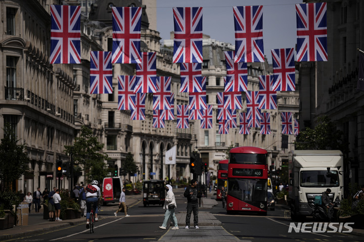 [런던=AP/뉴시스]지난 5월18일 엘리자베스 2세 영국 여왕의 퇴치 70주년을 기념하기 위해 영국 국기들이 내걸린 런던 리젠트 스트리트의 쇼핑가를 사람들이 지나가고 있다. 2022.7.20·