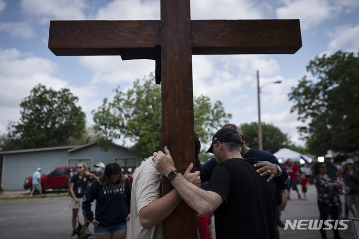 [유밸디( 미 텍사스주)=AP/뉴시스] 총격사건으로 19명의 어린이와 교사 2명이 살해된 텍사스 유밸디의 롭 초등학교 앞에 30일 디트로이트에서 나무십자가를 들고 온 조문객들이 기도를 하고 있다. 