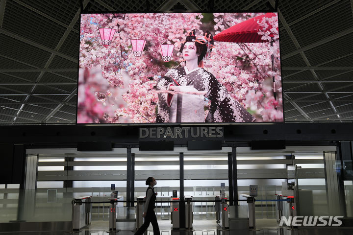 [도쿄=AP/뉴시스]일본 정부가 9월7일부터 일일 입국자수 상한을 현재 2만명에서 5만명으로 높이기로 방침을 정했다. 가이드 없는 외국인 패키지투어(단체여행)도 허용된다. 자료사진은 한 항공사 직원이 지난 6월10일 나리타 국제공항에서 일본 관광을 홍보 영상을 보면서 걷고 있는 모습. 2022.08.31.