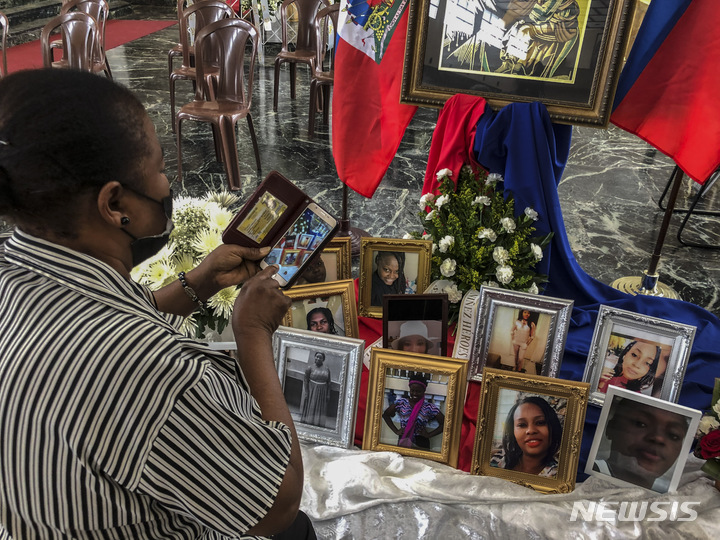 [산후안( 푸에르토리코)= AP/뉴시스]6월 15일 푸에르토 리코의 산후안 성당 앞에 놓인 11명의 아이티 여성과 소녀들 사망자 사진들 앞에서 한 여성이 휴대전화로 이를 촬영하고 있다. 이들은 지난 달 밀항선 보트가 전복되면서 숨진 뒤로 합동 장례식과 매장식이 치러졌다.