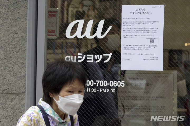 [도쿄=AP/뉴시스] 일본 수도 도쿄에서 4일 코로나19 예방을 위해 마스크를 착용한 시민이 휴대전화 장애 공지를 붙인  KDDI 점포 "au" 입구 앞을 지나가고 있다. 이날 통신 이상으로 인해 KDDI 가입자 4000만명 가까이 불편을 겪었다. 2022.07.06 