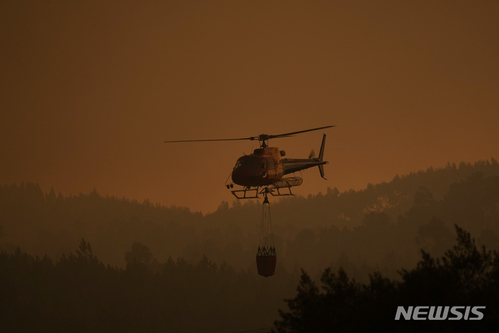 [안시아우=AP/뉴시스] 13일(현지시간) 포르투갈 중부 안시아우 인근 벰포스타 마을에서 소방 헬기 한 대가 짙은 연기 사이를 낮게 비행하며 화재 진압용 물을 옮기고 있다. 2022.07.14.